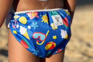 A child wearing a reusable swim nappy with a colorful beach and pool print, featuring characters and summer themes.